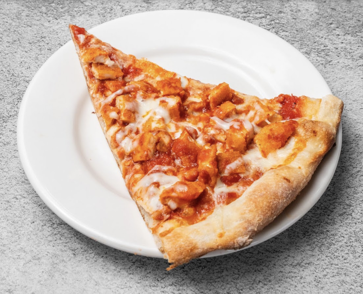 A specialty chicken pizza slice served on a white plate